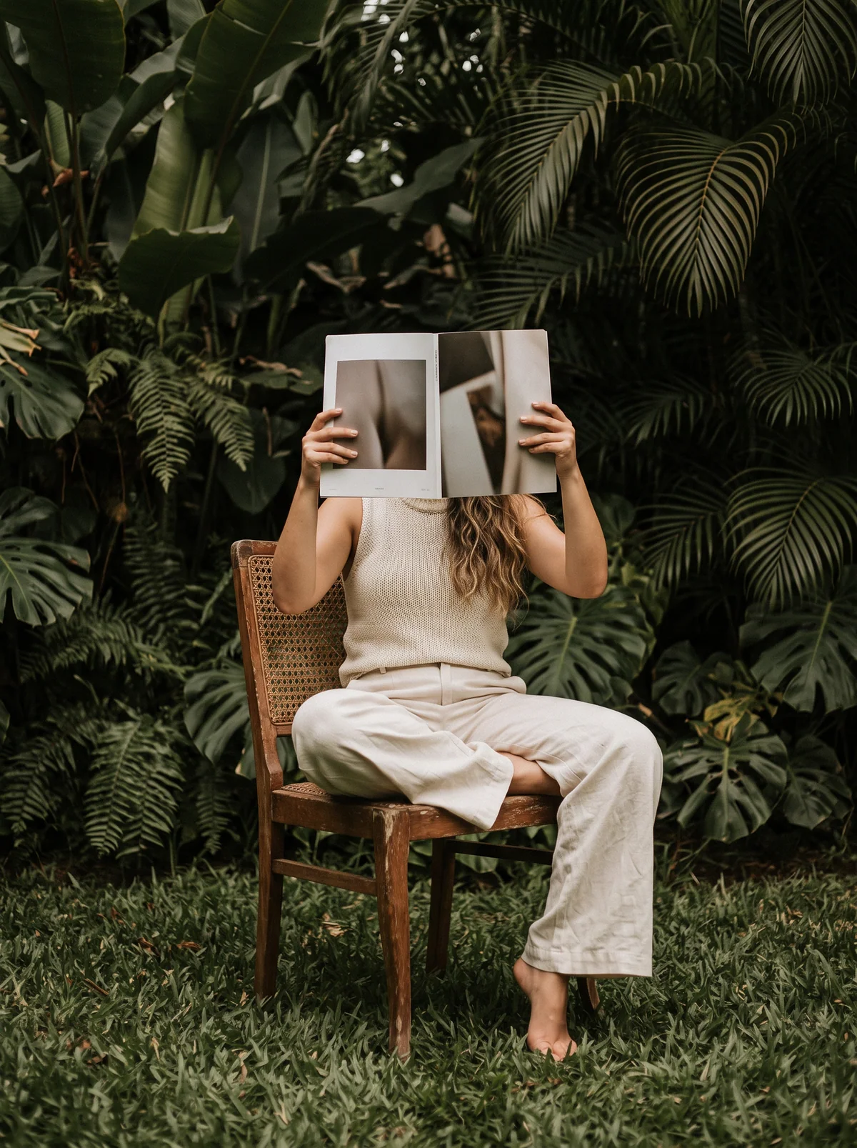 Ana Avilés leyendo una revista de arquitectura en una silla de madera y rattan, rodeada de plantas